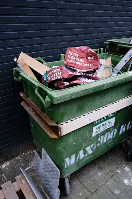 In front of a traditional brick-built restaurant with large glazed windows and wooden framing painted in deep red, a black commercial waste bin marked 'Commercial Waste Only' is positioned on the side